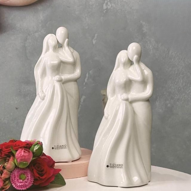 Eine weiße Keramikfigur eines eng umschlungenen Paares in eleganter Kleidung.