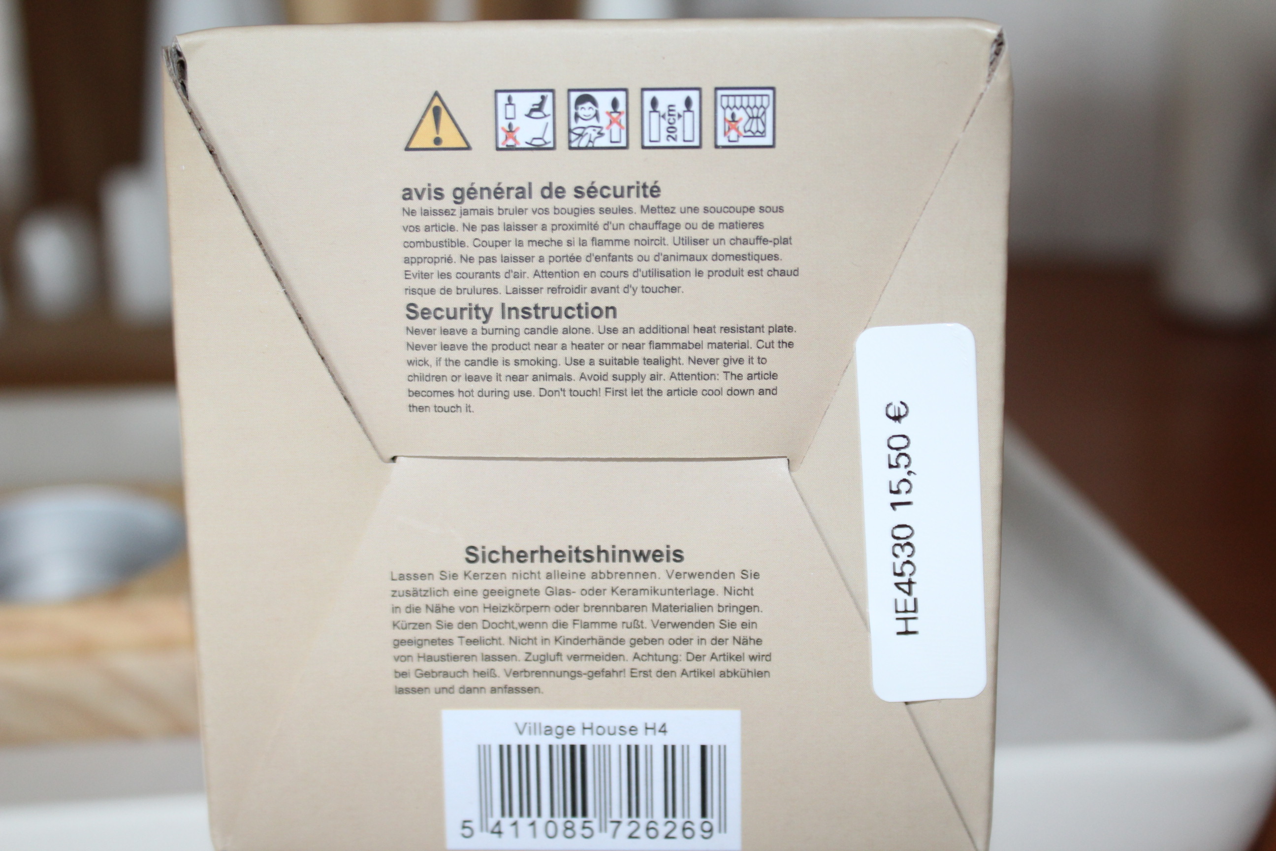 Nahaufnahme einer Kerzenschachtel mit Sicherheitshinweisen in mehreren Sprachen, darunter Englisch, Französisch und Deutsch, und einem Preisschild von 15,50 €.