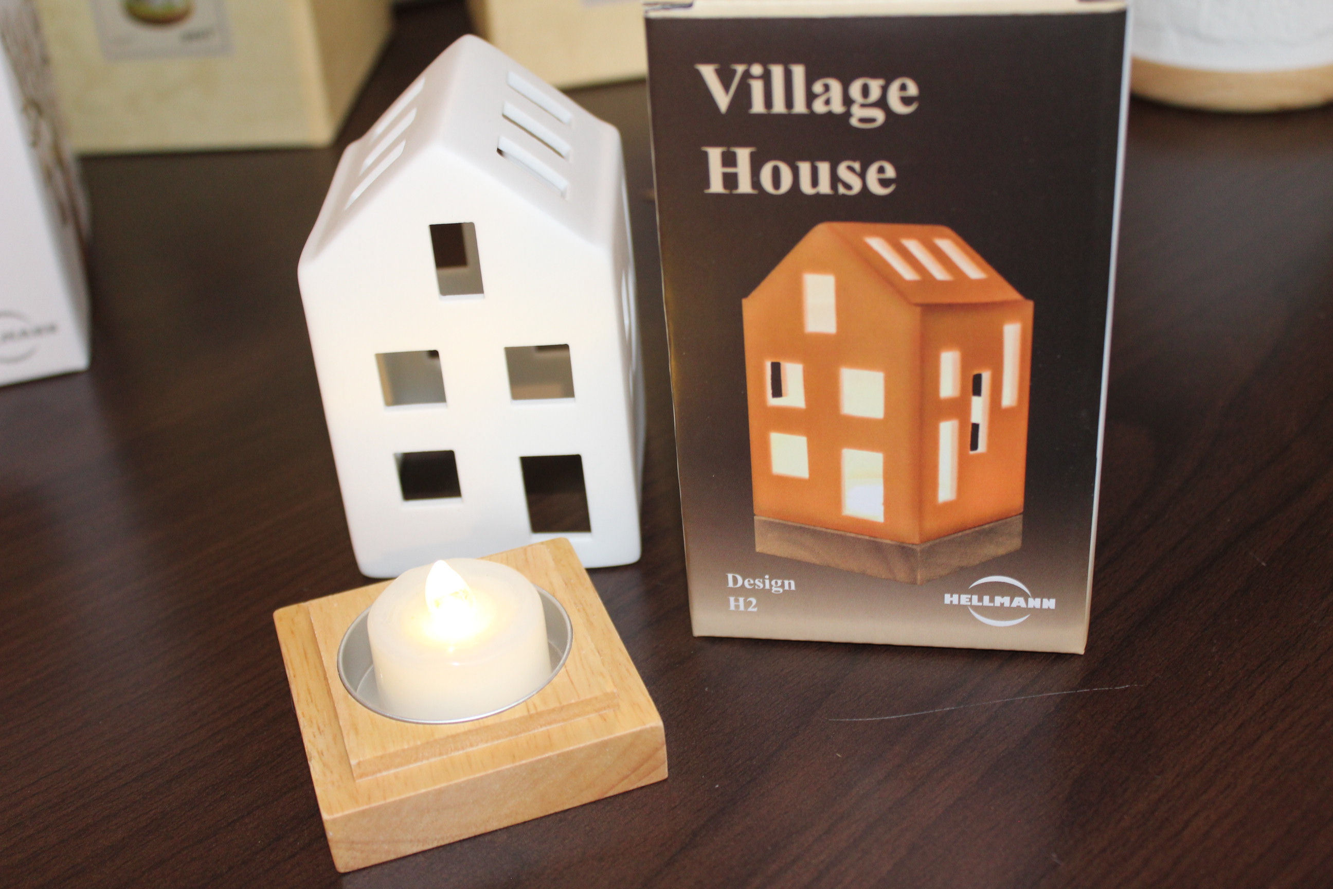 Dekorativer Dorfhaus-Kerzenhalter auf einem Holztisch mit Verpackungsbox.