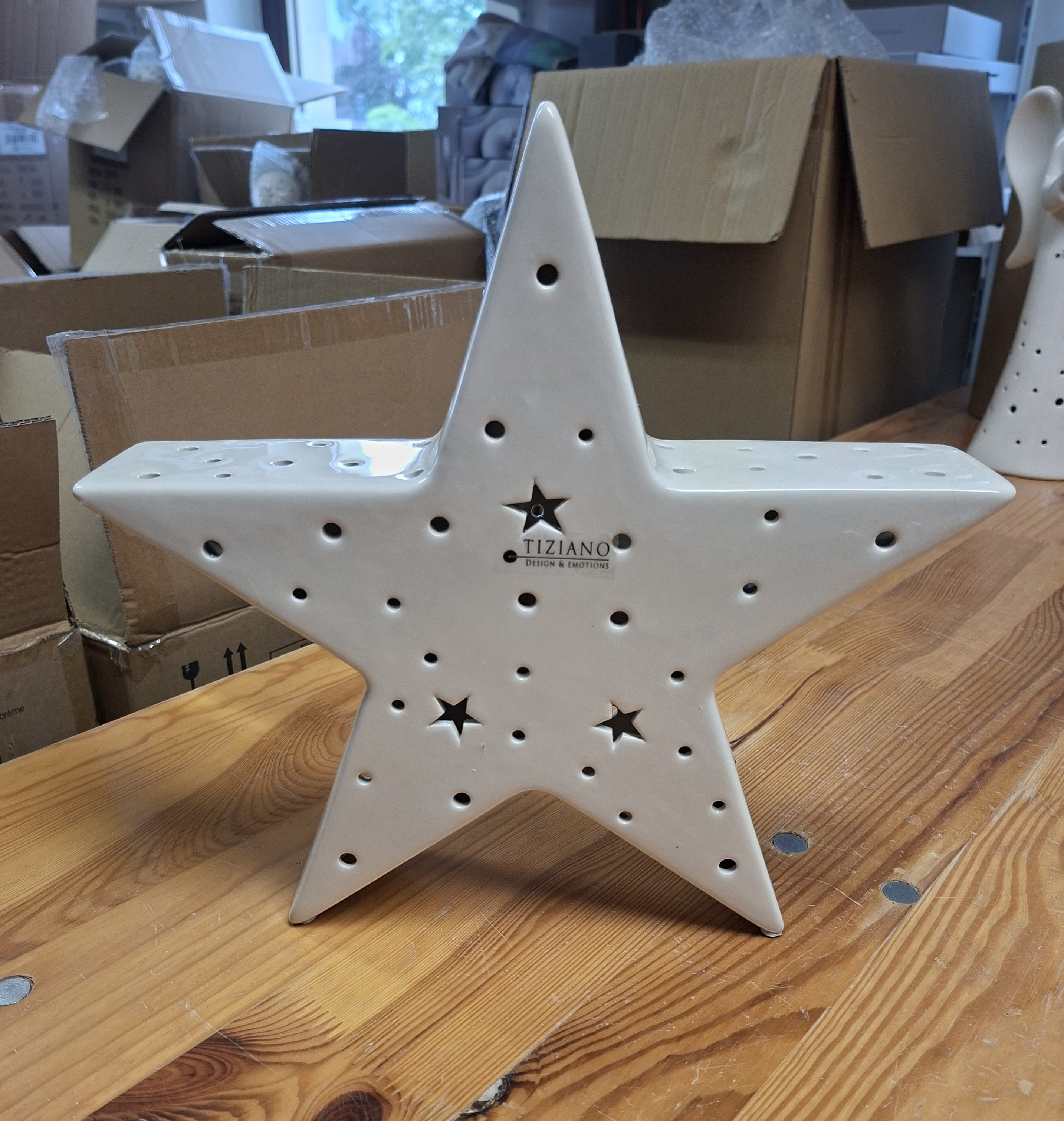 Eine dekorative sternförmige Lampe aus weißer Keramik von Tiziano Design & Emotions mit perforierten Löchern für Licht, ausgestellt auf einem Holztisch in einer Lagerhalle.