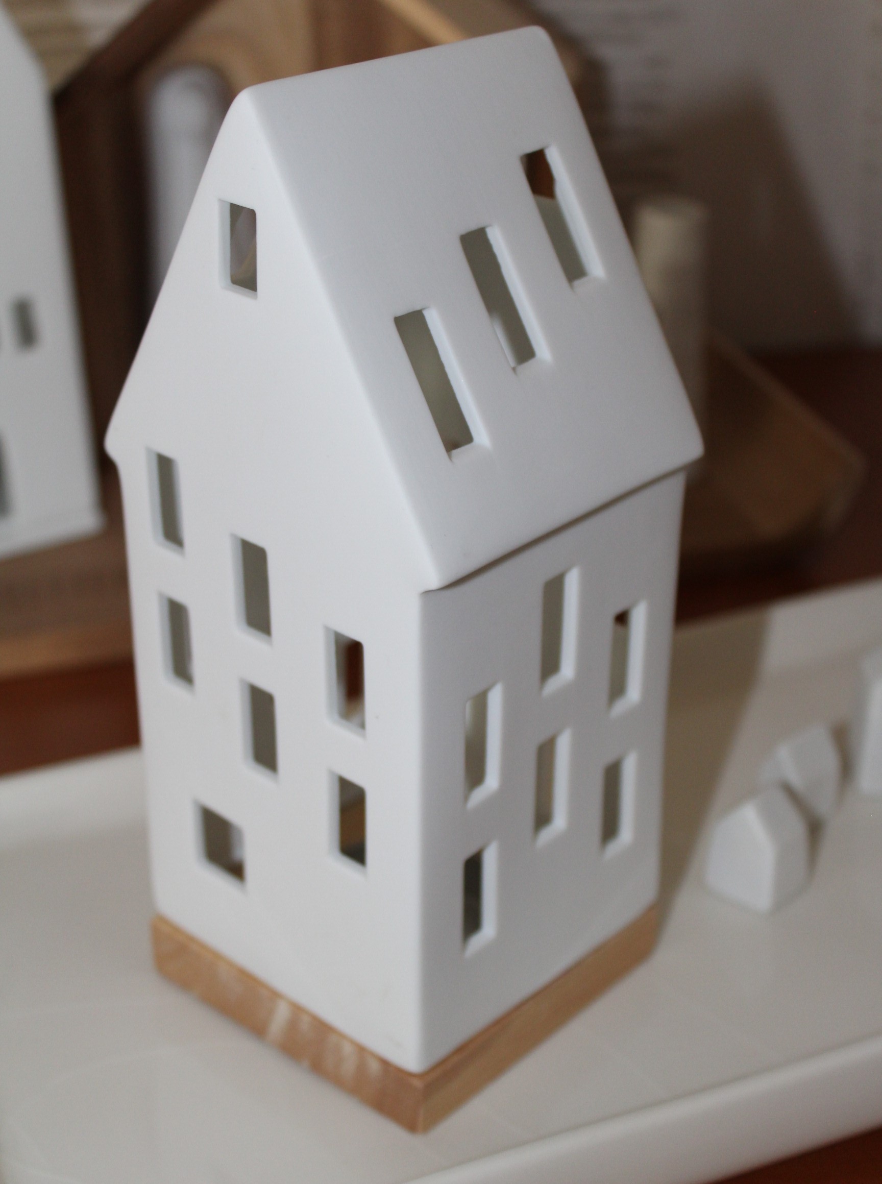 Eleganter Teelichthalter aus weißer Keramik mit rechteckigen Ausschnitten und einem Sockel aus Naturholz, perfekt für die Inneneinrichtung und Umgebungsbeleuchtung.