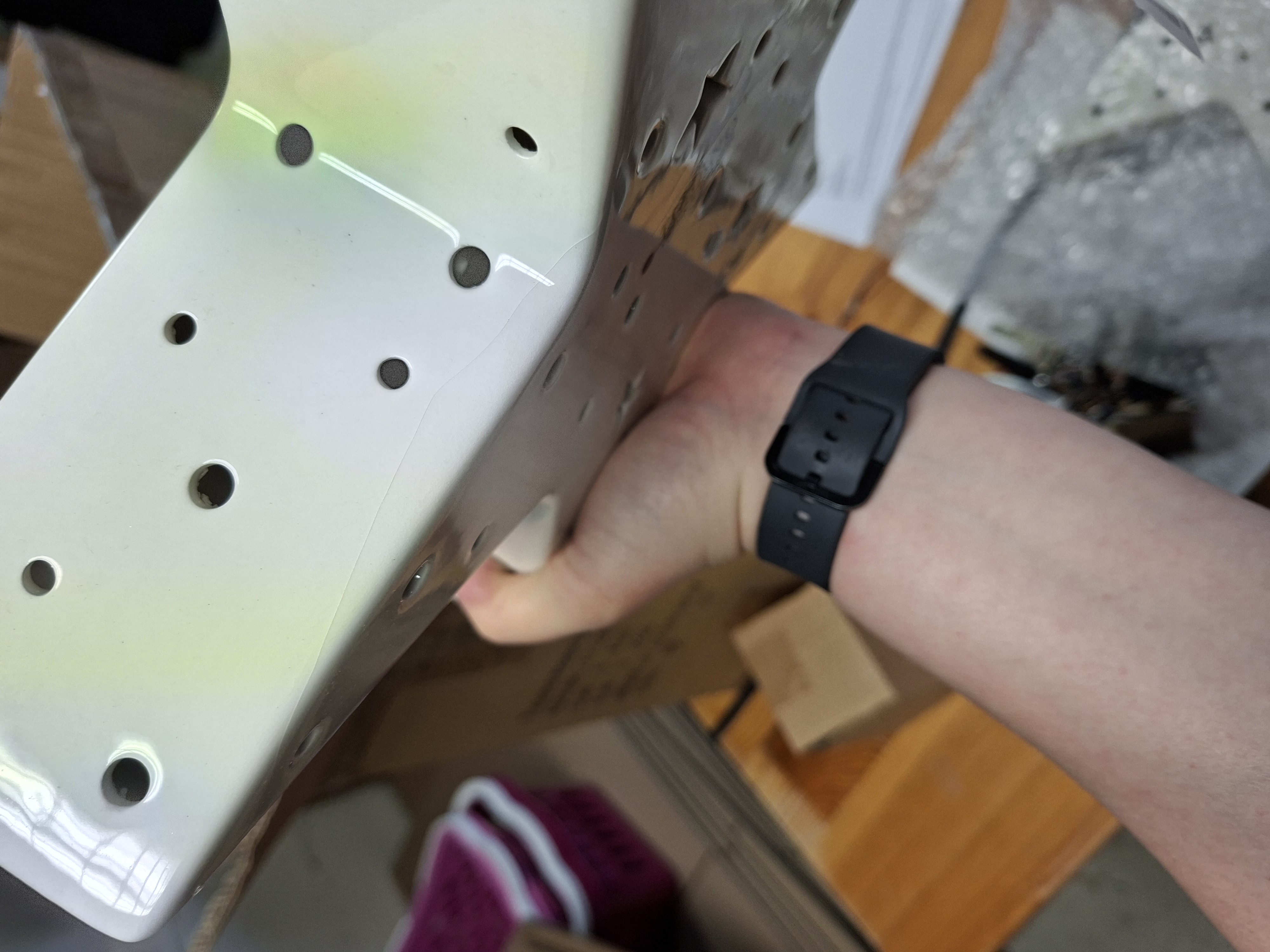 Eine Person hält ein weißes Keramikobjekt mit mehreren Löchern und zeigt dessen Design und Textur. Der Hintergrund besteht aus Verpackungsmaterialien und einer Holzoberfläche.
