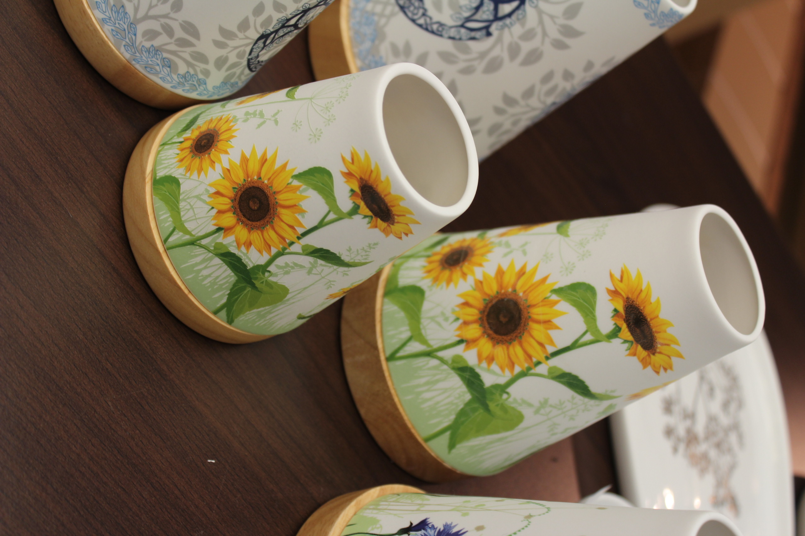 Weiße Keramikvasen mit Sonnenblumenillustrationen auf einem Holztisch.