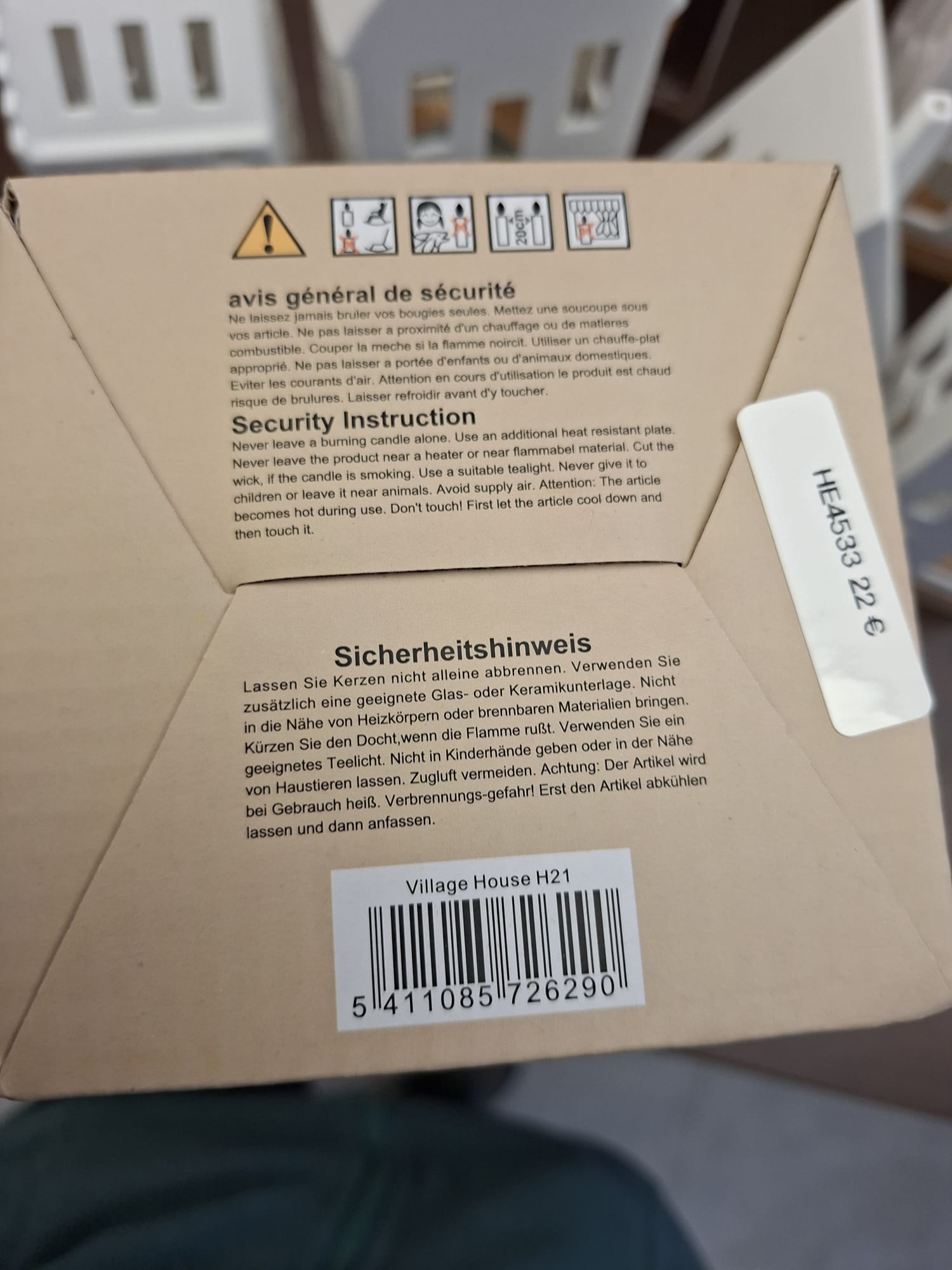 Nahaufnahme einer Produktverpackung mit Sicherheitshinweisen in Französisch, Englisch und Deutsch sowie Warnsymbolen und einem Barcode. Die Box ist hellbraun mit schwarzem Text.
