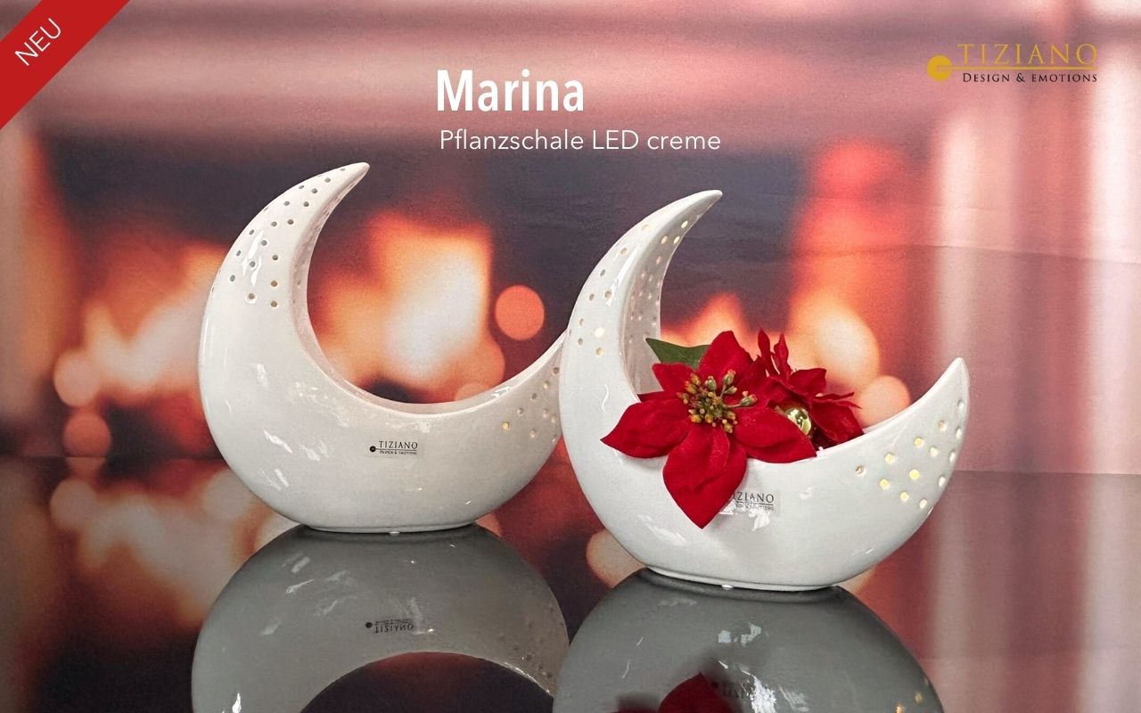 Zwei halbmondförmige Keramik-Pflanzgefäße in Cremefarbe mit dekorativen Ausschnitten und Tiziano-Branding, präsentiert auf einer reflektierenden Oberfläche vor einem warmen, verschwommenen Hintergrund mit einer roten Weihnachtssternblume in einem.