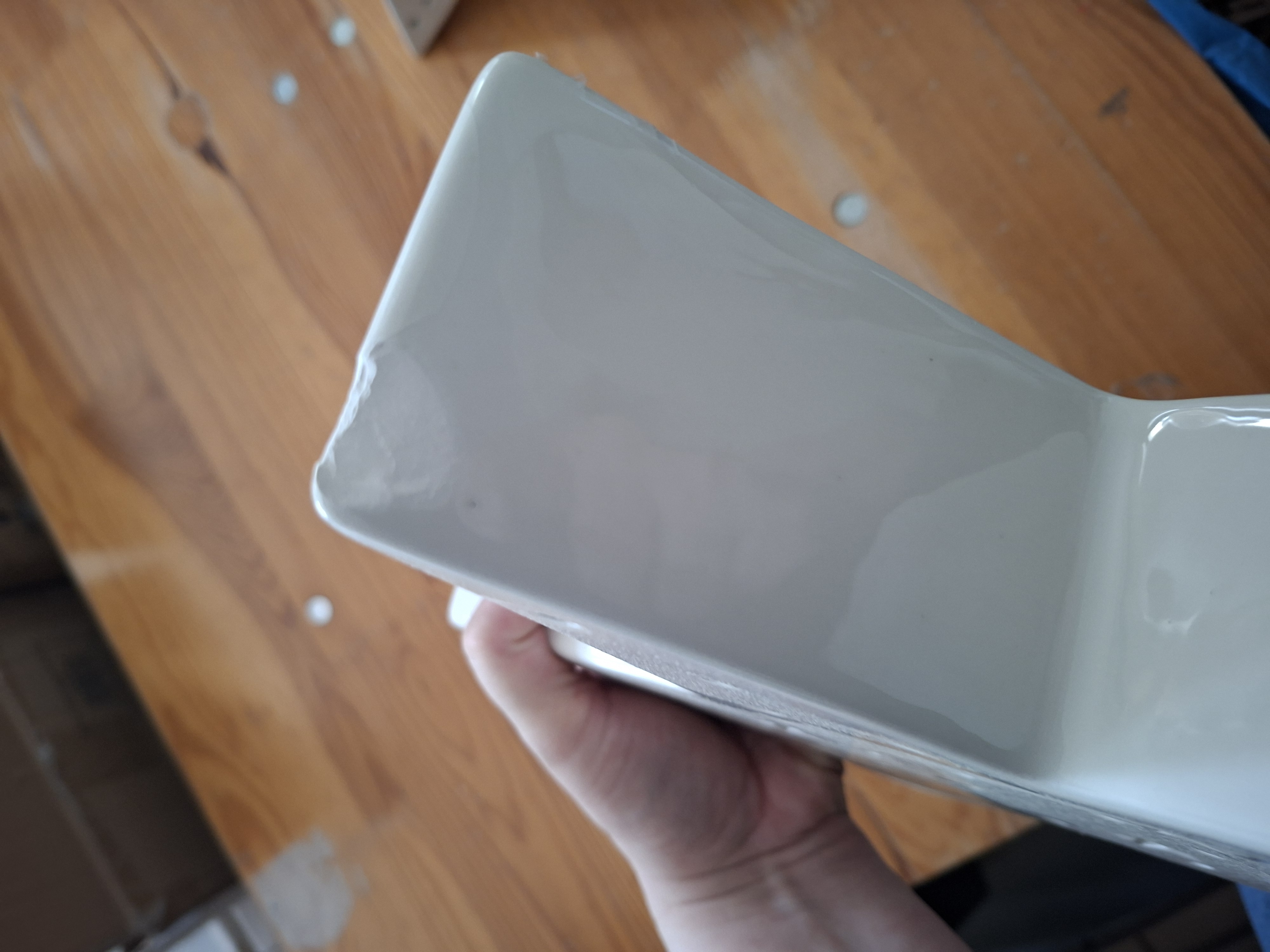 Eine Nahaufnahme eines weißen Keramikobjekts, das in einer Hand gehalten wird. Sie zeigt einen sichtbaren Abplatzer und eine Beschädigung an der Eckkante des Materials, was auf ein Qualitätskontrollproblem oder einen Produktfehler hinweist.