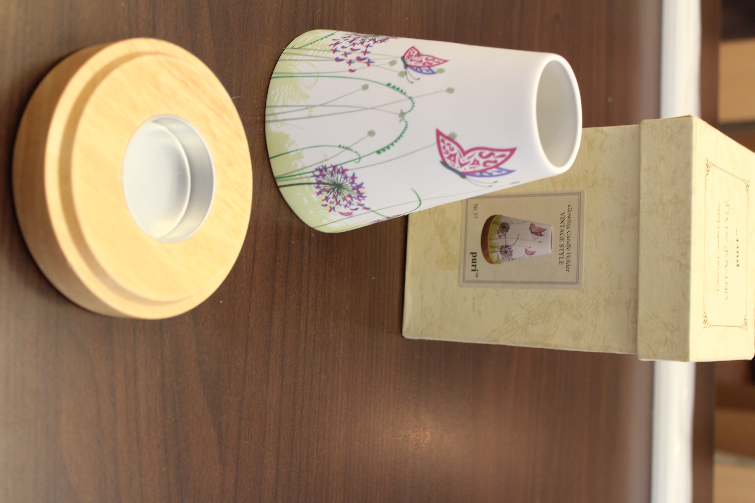 Kerzenhalter im Vintage-Stil mit Blumen- und Schmetterlingsdesign neben einer passenden Schachtel auf einem Holztisch.