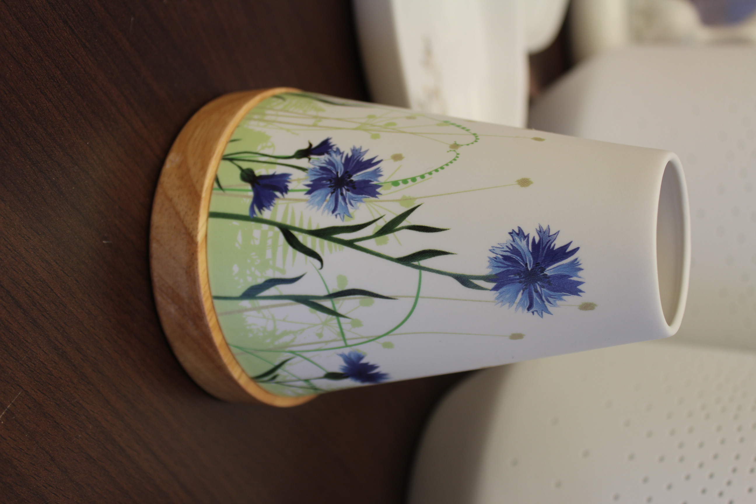 Weiße kegelförmige Keramikvase mit blauem Blumenmuster auf einem Holzsockel auf einer dunklen Holzoberfläche.