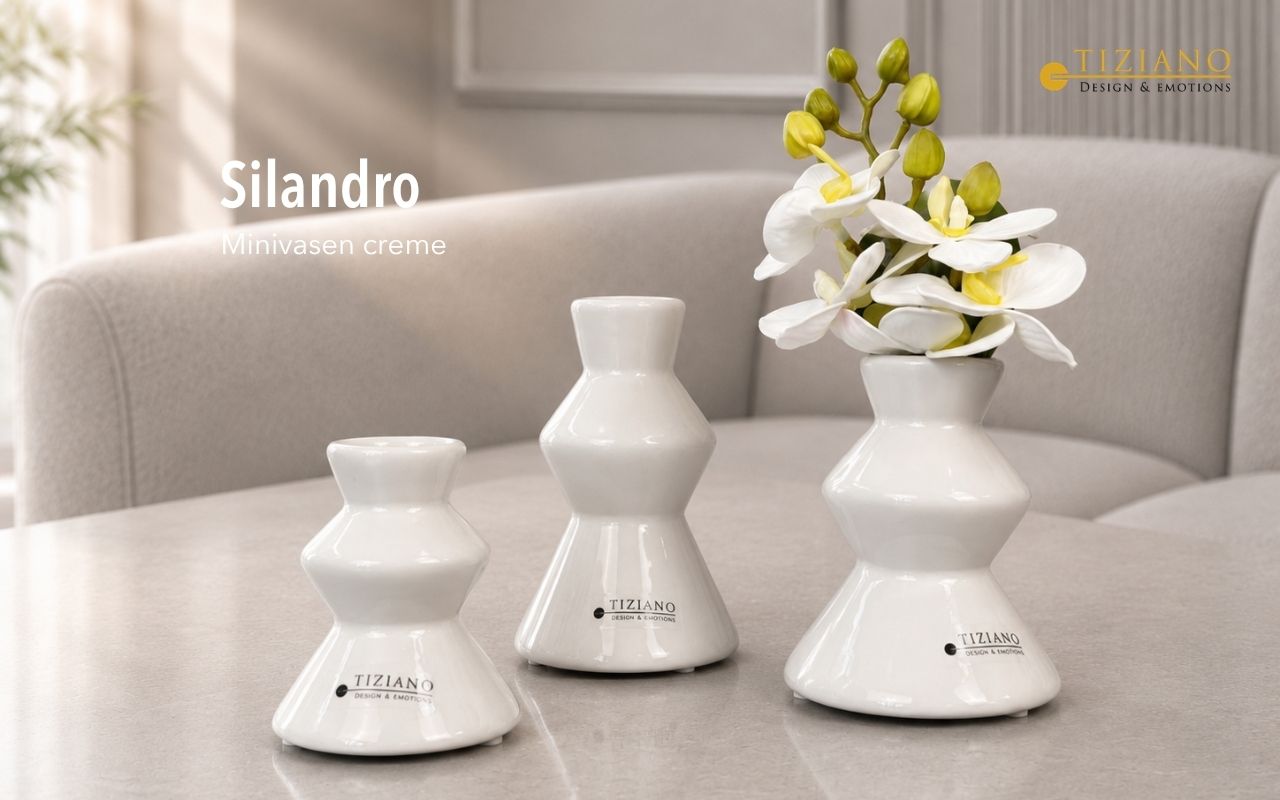 Drei cremefarbene, sanduhrförmige Keramikvasen unterschiedlicher Größe auf einem Tisch angeordnet, wobei die größte Vase einen Zweig weißer Orchideen enthält, vor einem weichgezeichneten Wohnzimmerhintergrund.