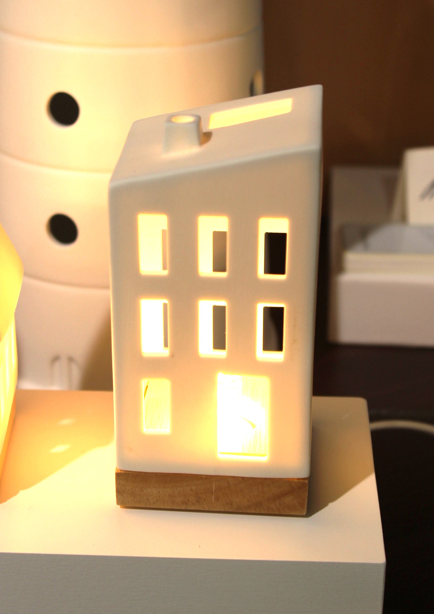 Dekorative hausförmige Keramiklampe mit warmem Lichtschein auf dem Ausstellungsregal.