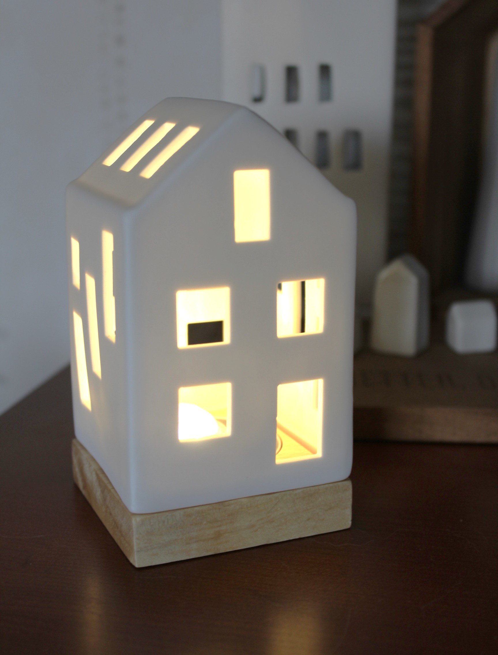 Elegante weiße Keramiklaterne in Hausform mit warm leuchtenden Lichtern, perfekt für die Inneneinrichtung und schafft eine gemütliche Atmosphäre. Verfügt über ein minimalistisches Design mit ausgeschnittenen Fenstern und Dachlüftungsöffnungen und ruh