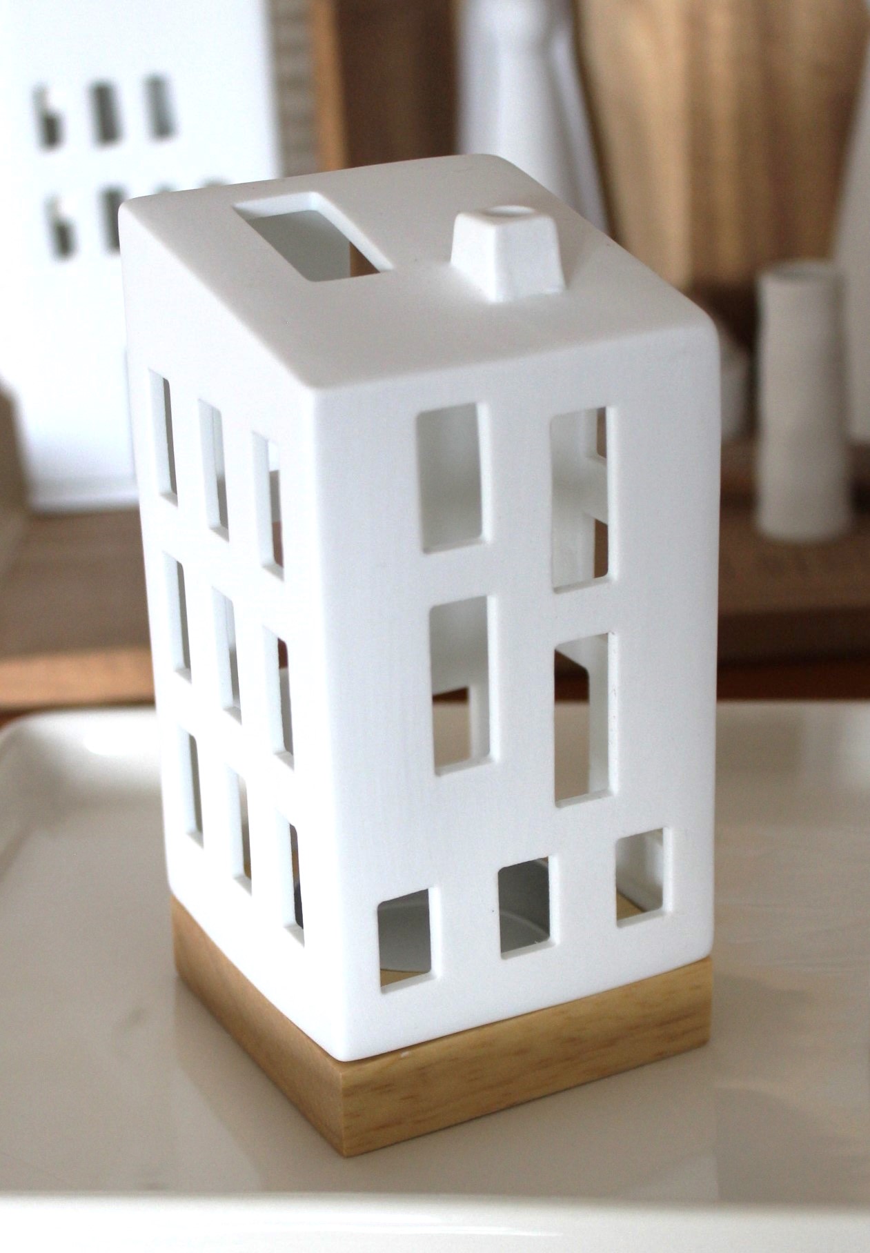 Moderner hausförmiger Kerzenhalter aus weißer Keramik mit Sockel aus Naturholz, ideal für die Inneneinrichtung, der jedem Raum ein minimalistisches und warmes Ambiente verleiht.