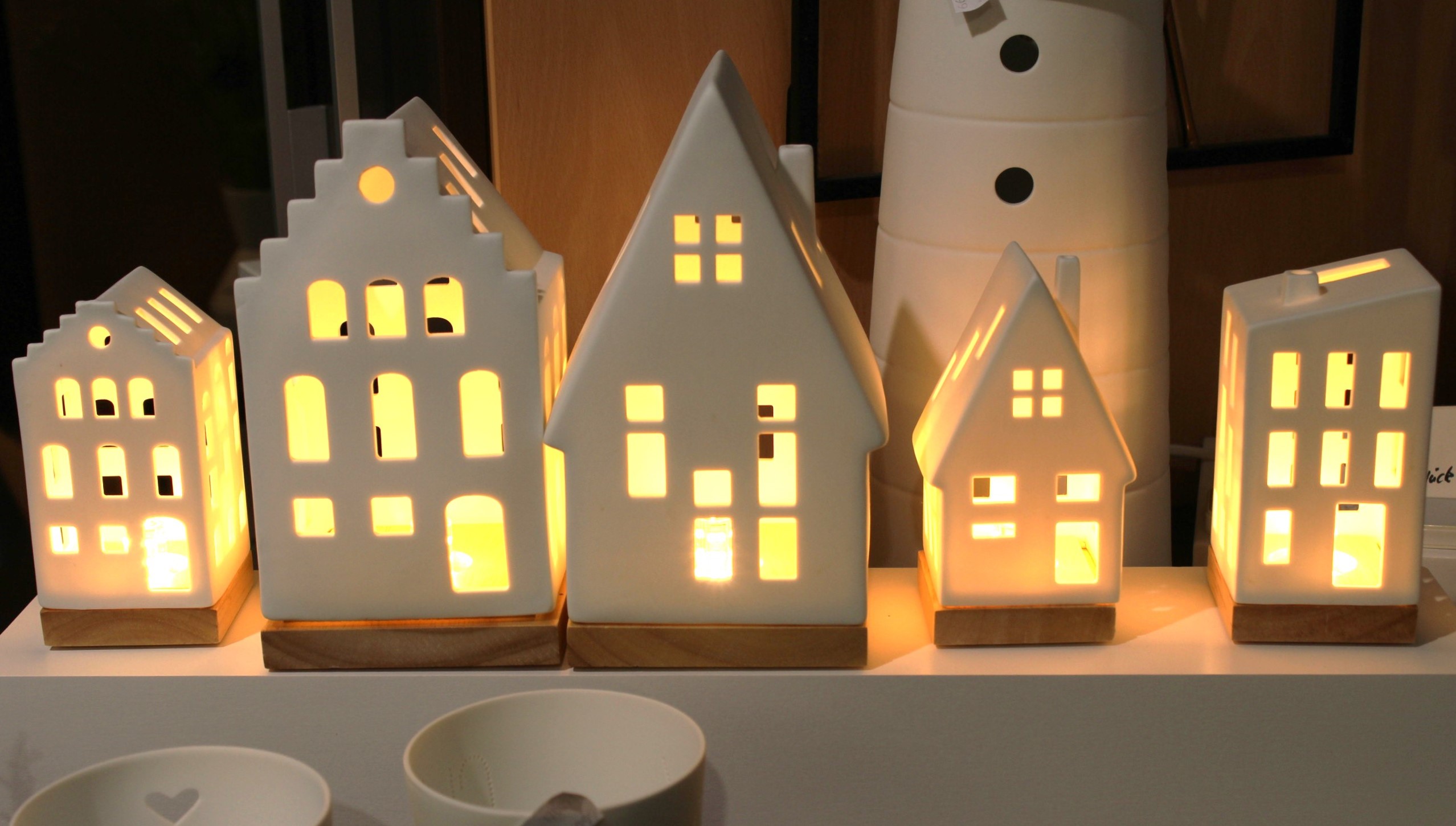 Beleuchtete Hauslaternen aus Keramik auf einem Regal sorgen für eine gemütliche und warme Atmosphäre.