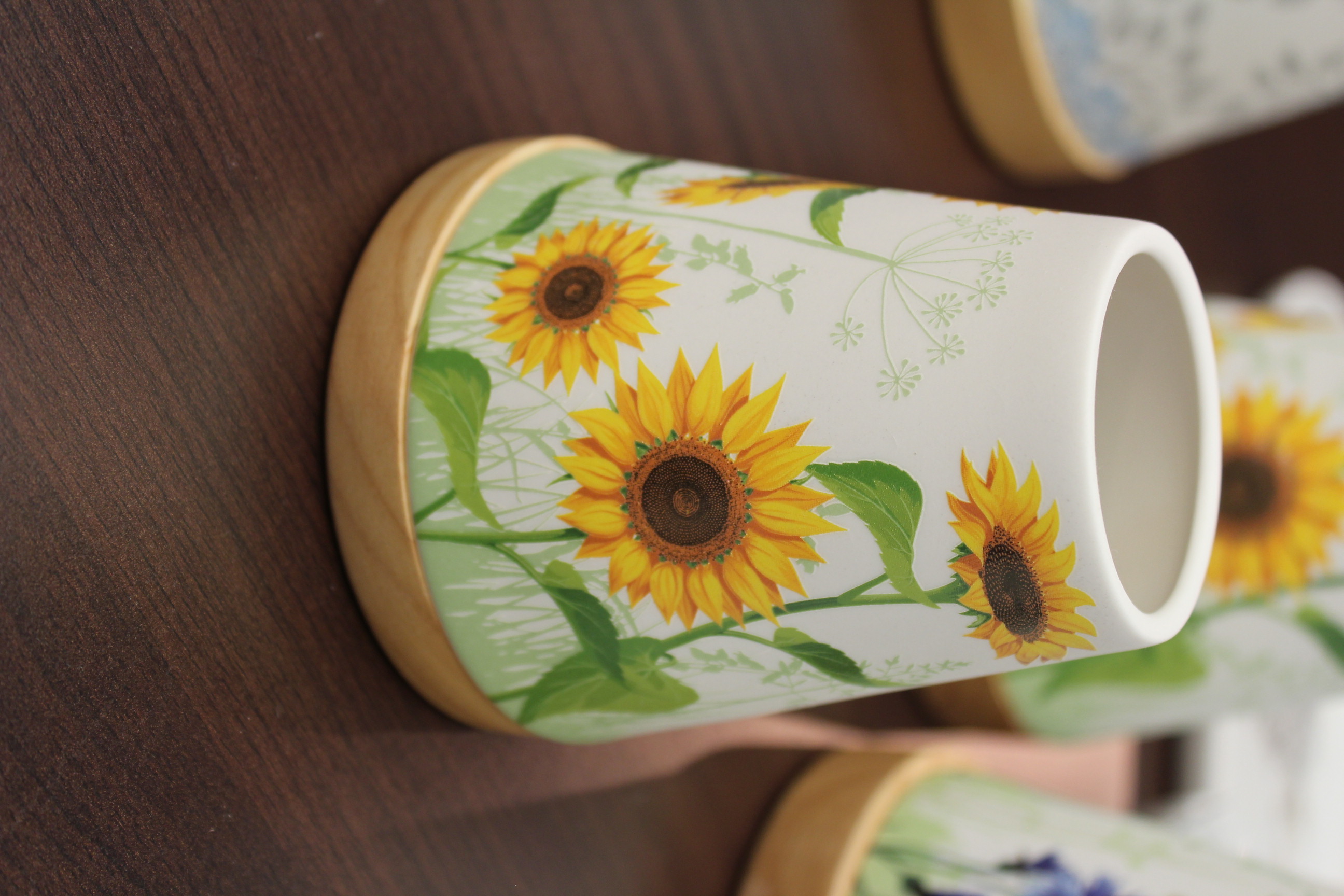 Dekorative Keramikvase mit lebendigem Sonnenblumendesign auf einem Tisch aus dunklem Holz.