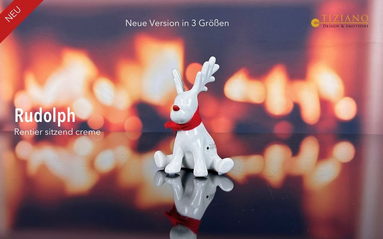 Eine weiße Keramik-Rentierfigur namens Rudolph, die einen kleinen roten Schal trägt und eine rote Nase hat, sitzt auf einer reflektierenden Oberfläche vor einem verschwommenen, warmen Kaminhintergrund.