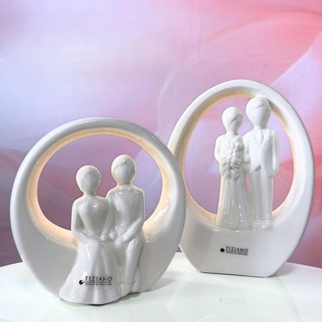 Dekorative Figurenset von Tiziano mit Paar- und Hochzeitsmotiv in eleganter Keramik. Ein Hochzeitspaar sitzt oder steht mittig in einen ovalen bzw. eiförmigen Keramikring.