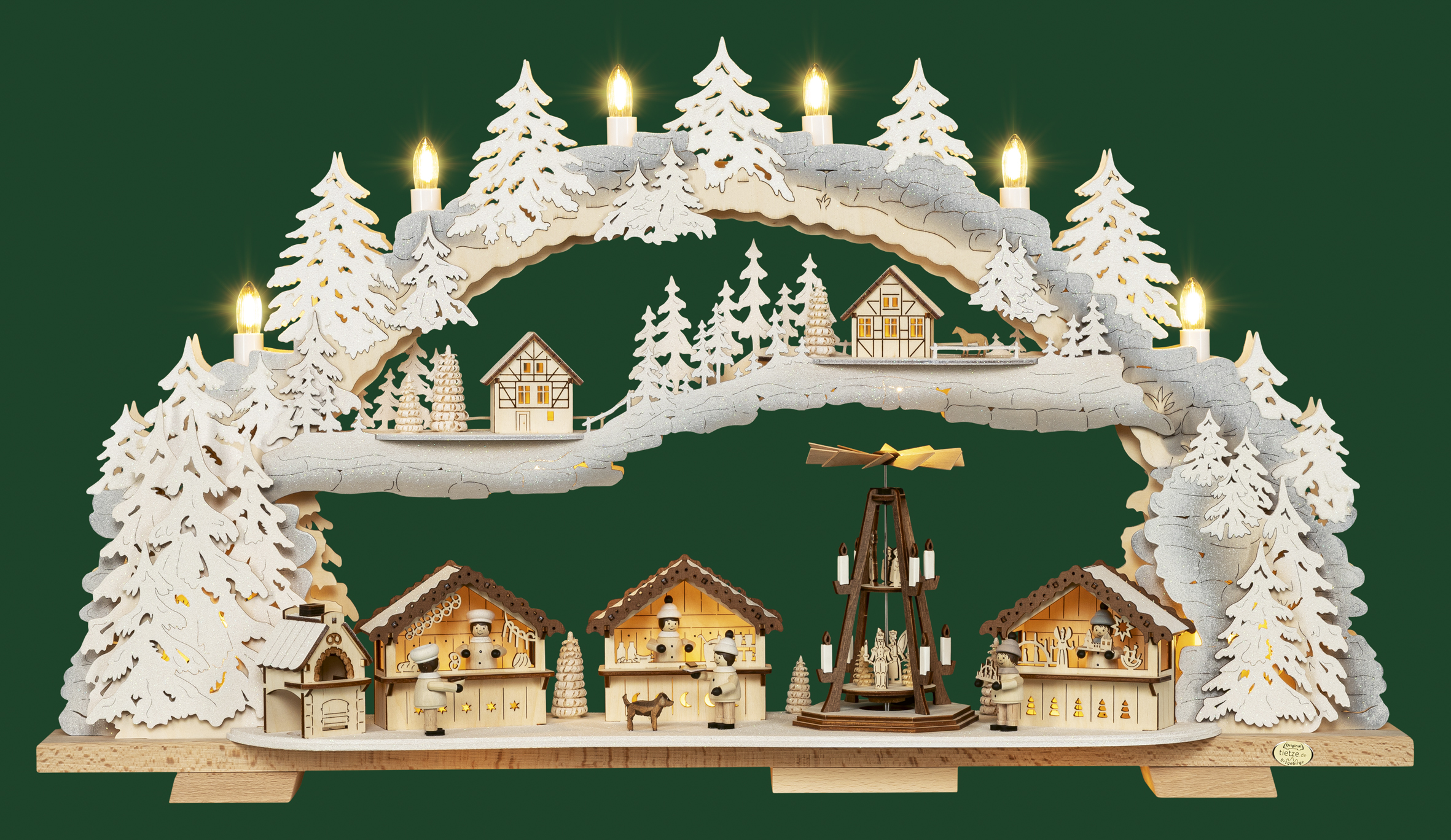 Variabler LED-Schwibbogen von Tietze Erzgebirgsdesign GmbH, 70 cm, mit einer detaillierten Weihnachtsmarktszene mit Holzständen, einer zentralen Pyramide, verschneiten Bäumen und warmer LED-Beleuchtung vor dunkelgrünem Hintergrund.