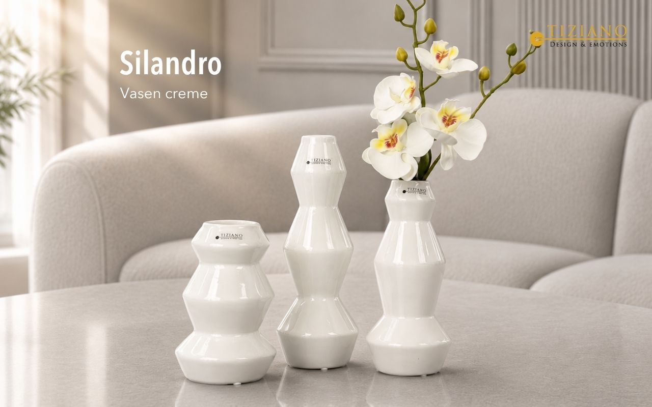 Drei moderne, cremefarbene Silandro-Keramikvasen mit geometrischem Stapelmuster auf einem Tisch angeordnet, wobei eine Vase einen weißen Orchideenzweig hält, vor einem verschwommenen Wohnzimmerhintergrund.